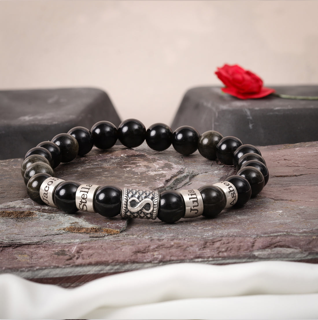 Personalized obsidian bracelet featuring engraved names and silver infinity charm
